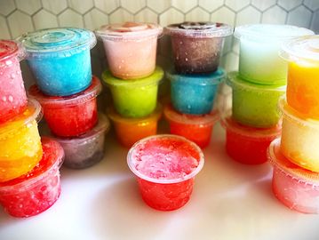 Colorful frozen treats in small plastic cups with lids.