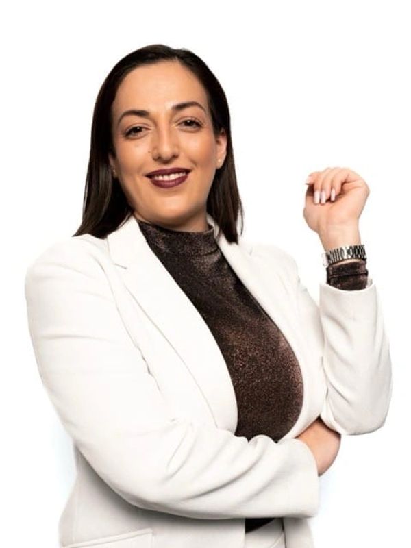 Confident woman in white blazer and dark top posing with a smile.