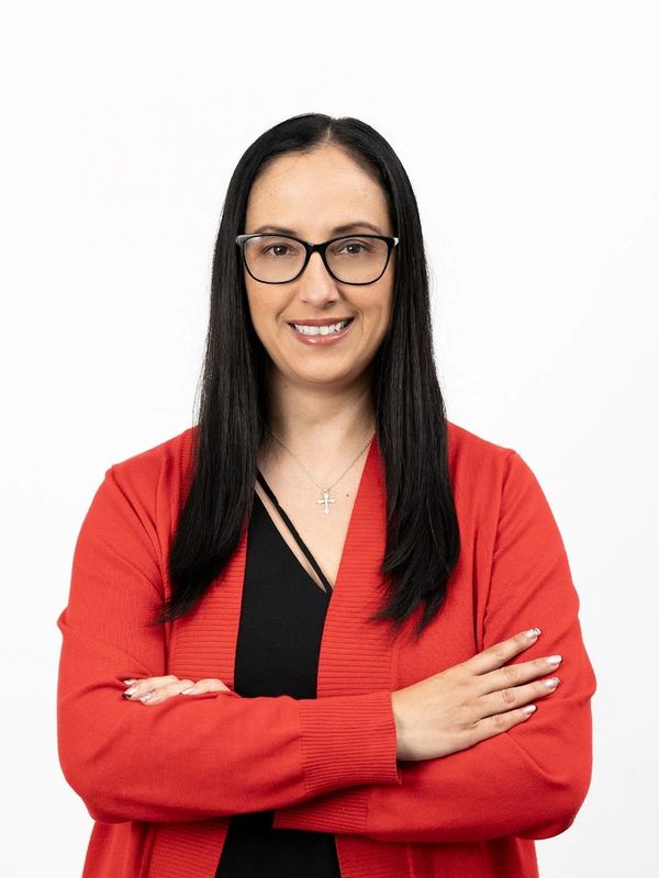 Confident woman with glasses and long hair wearing a red cardigan.