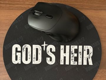 Black mouse on a mousepad reading 'GOD'S HEIR'.