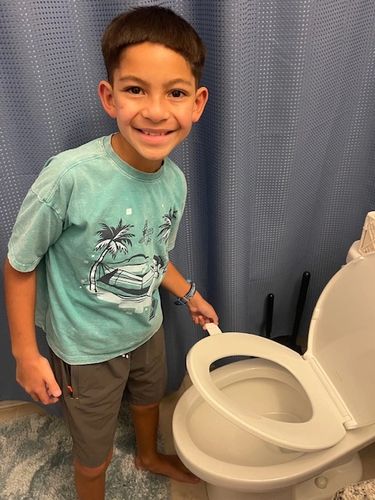 A boy smiling while lifting a toilet seat in a bathroom.