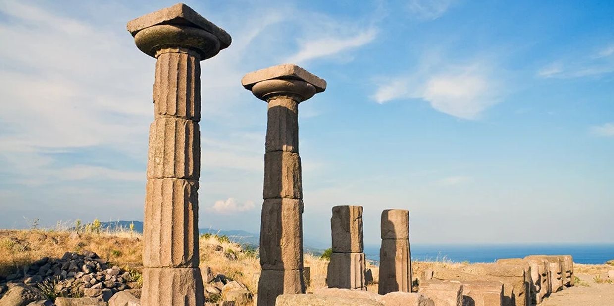 Ancient stone columns standing under a blue sky near the sea.