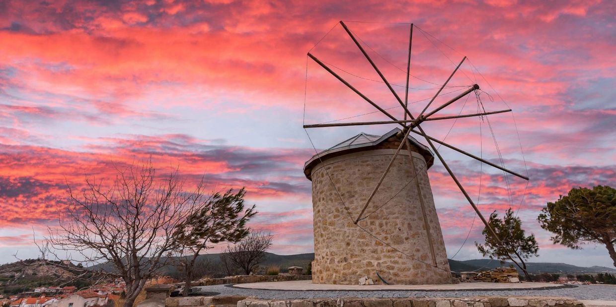 Historic stone windmill under a vibrant pink sunset sky.