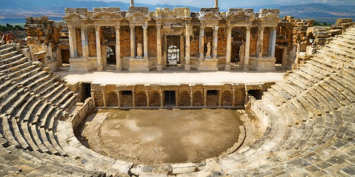 Ancient Roman amphitheater with stone seating and ornate stage backdrop.