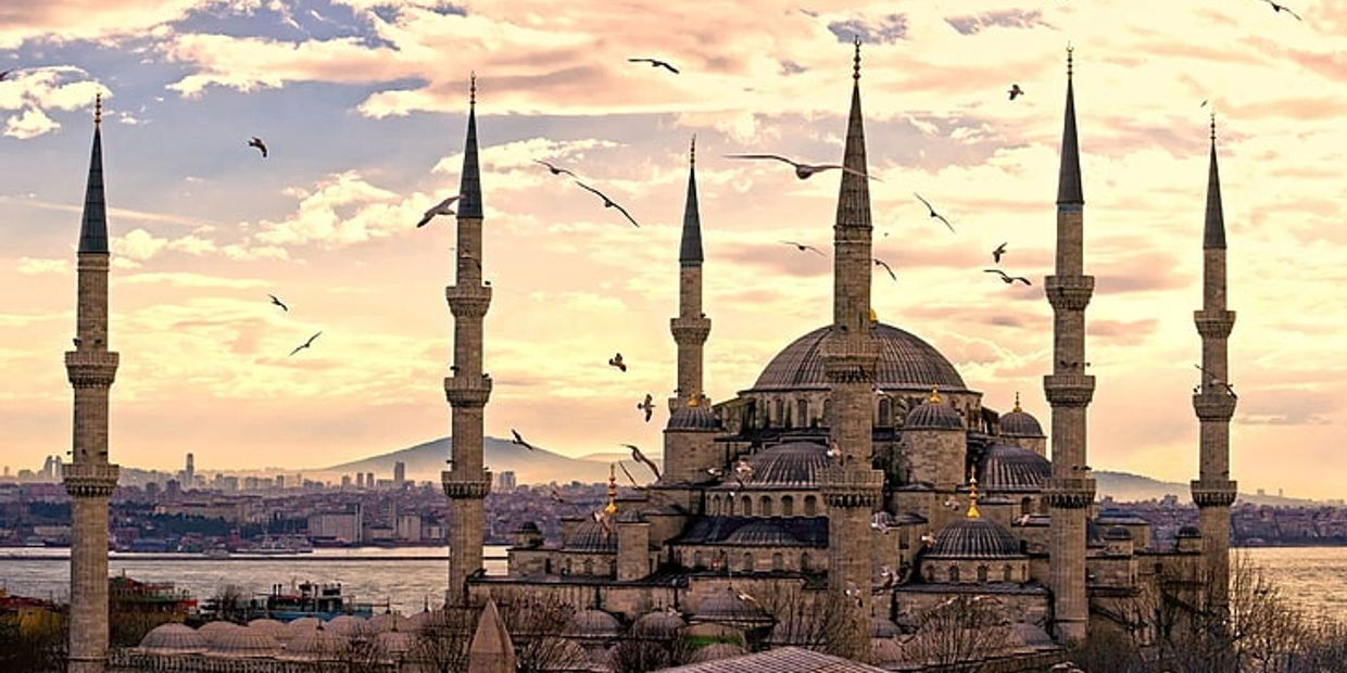 The iconic mosque with six minarets under a colorful sky with flying birds.