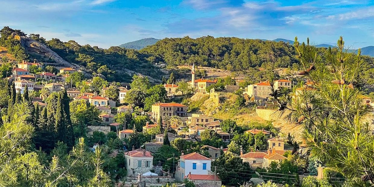 A scenic hillside village with stone houses and lush greenery under a bright blue sky.