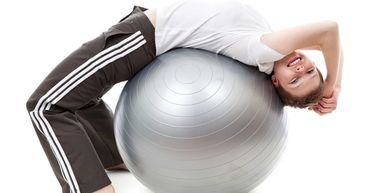 An adolescent boy bending backwards over an exercise ball to regulate his system.