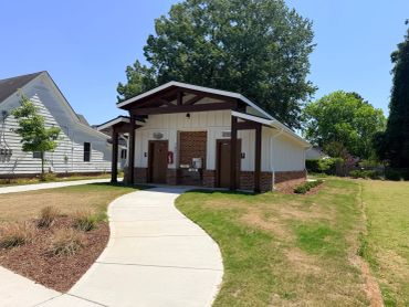 A small public restroom building with a curved sidewalk and green trees.