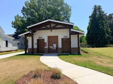 Small public restroom building with surrounding greenery and clear sky.