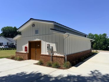 Small utility building with white siding and brick base on a sunny day.