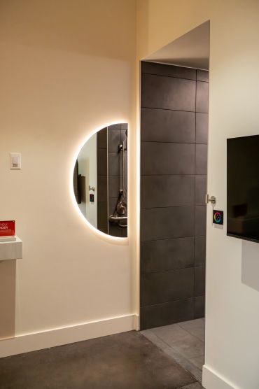 Modern interior with a round illuminated mirror and dark tiled doorway.