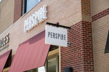 Storefront sign for Perspire on a brick building with red awning.