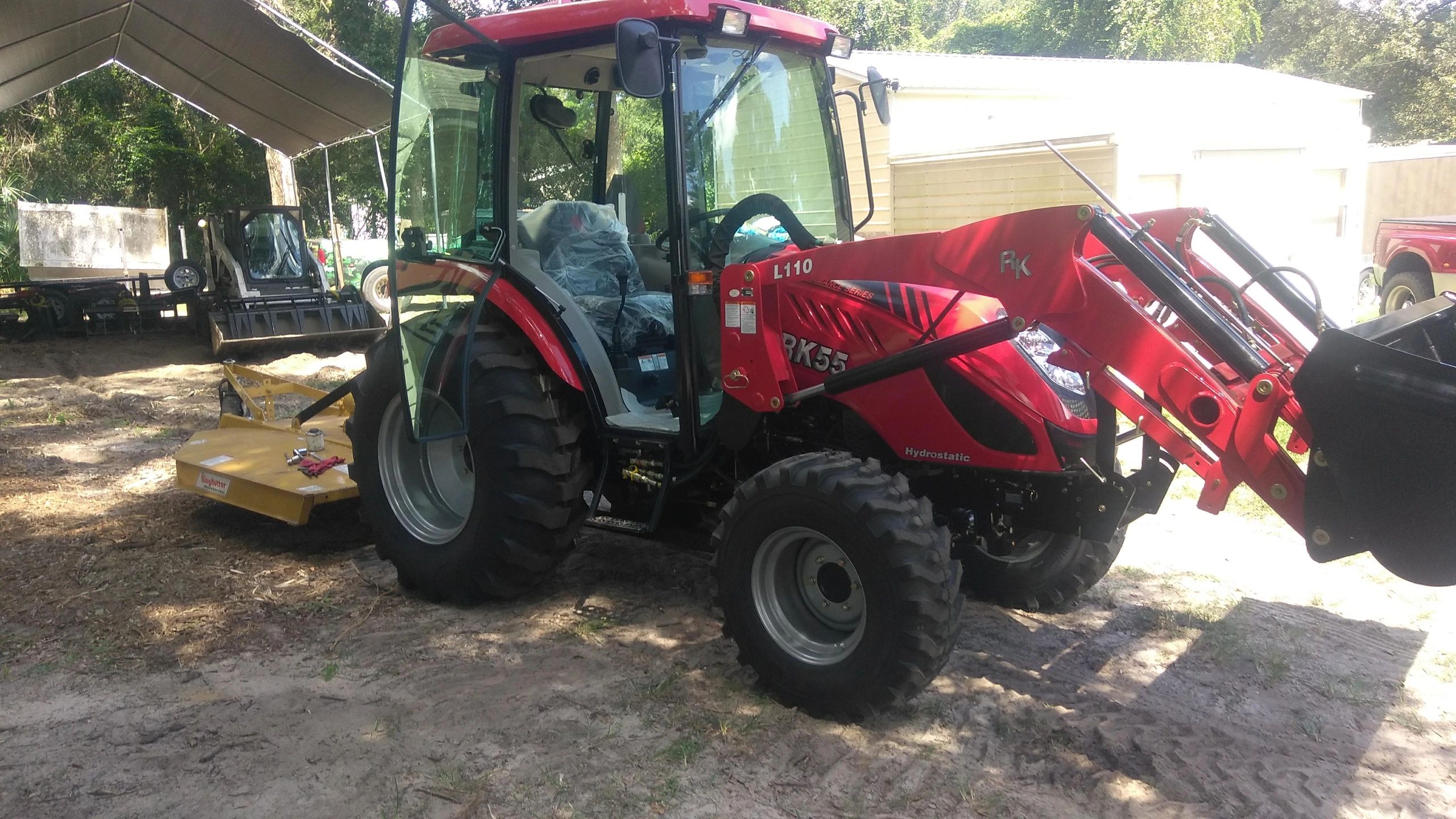 Red tractor with front loader and mower attachment parked outdoors.