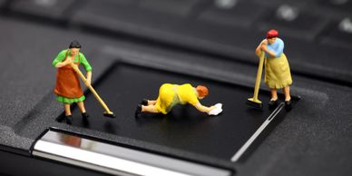 miniature housekeepers sweeping and mopping the keyboard on a laptop