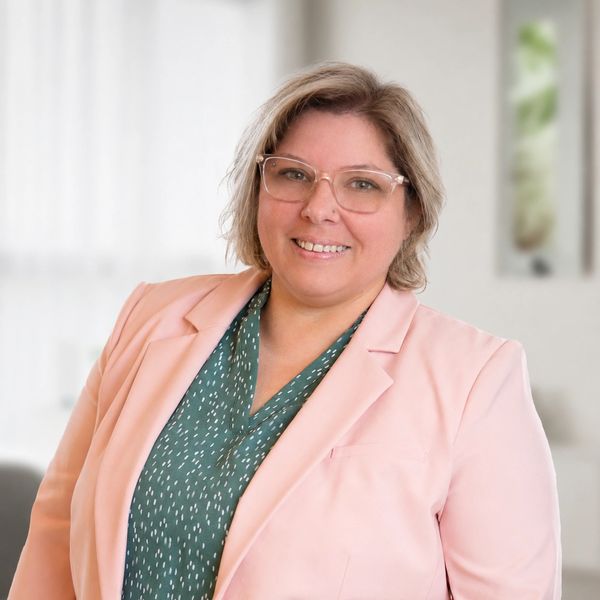 Woman smiling, wearing glasses and a pink blazer.