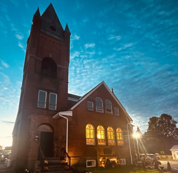 Historic church with stained glass windows glowing at dusk under a cloudy sky.