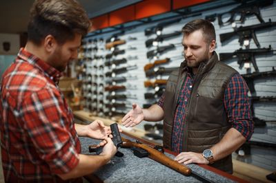 An employ gesturing to a client who is looking at a handgun. 