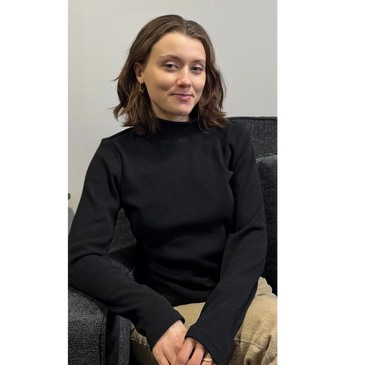 A woman in a black turtleneck sitting on a dark chair.