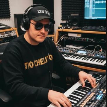 Man wearing headphones and sunglasses playing a keyboard in a music studio.