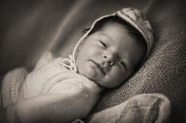 Black and white photo of a newborn baby in a knitted outfit and bonnet.