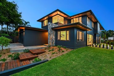 Modern two-story house with illuminated exterior and landscaped yard at dusk.
