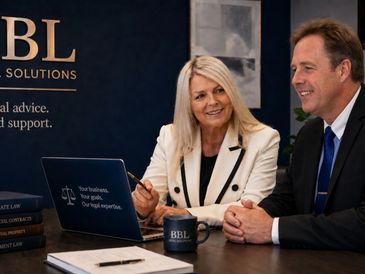Two professionals discussing business at a desk with a laptop and branded mug.