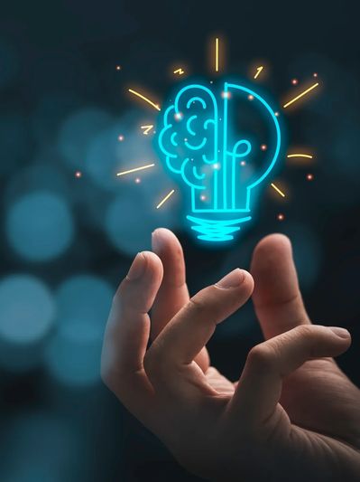 Hand holding a glowing light bulb with a brain symbol, symbolizing creativity and ideas.