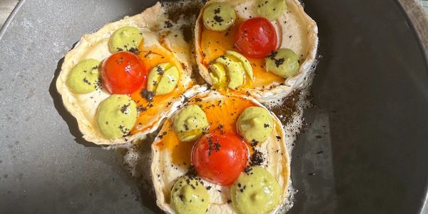 Three slices of baked cheese with cherry tomatoes and green sauce on a dark plate.