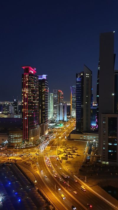 Nighttime cityscape with illuminated skyscrapers and busy roads.