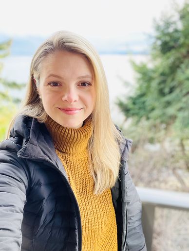 A woman in a yellow sweater and black jacket smiling outdoors.