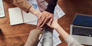 A team of people all put their hands to the centre to signifying a commitment to Teamwork 