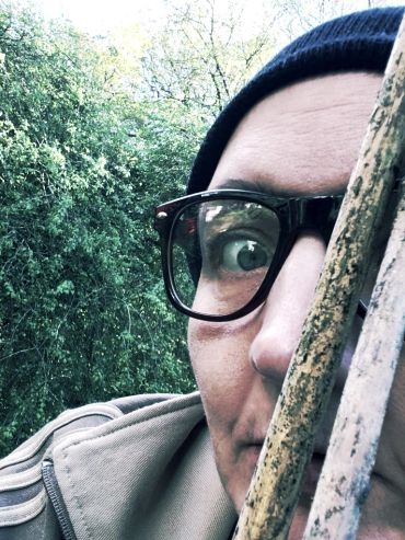 Close-up of a person peeking from behind wooden sticks outdoors.