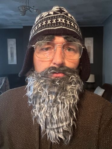 Person wearing a fake grey beard and glasses with a winter hat.