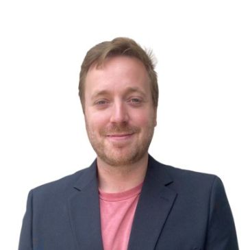 Smiling man in blazer and pink shirt.