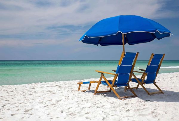 Two blue beach chairs and umbrella on white sand by turquoise ocean.