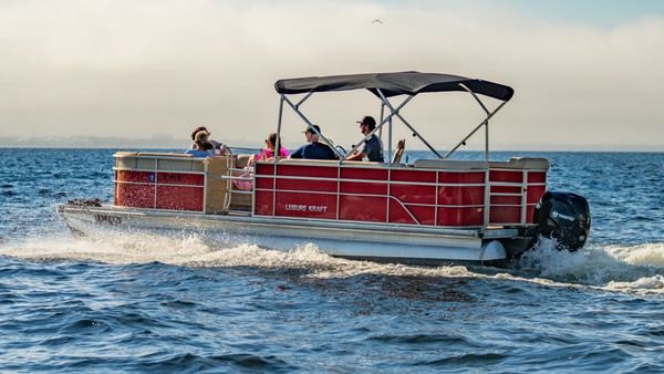 A group of people enjoying a ride on a red Leisure Kraft pontoon boat.