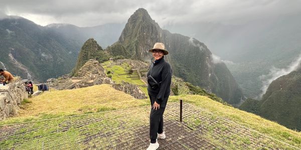 A woman posing at Machu Picchu with mountains and ruins in the background.