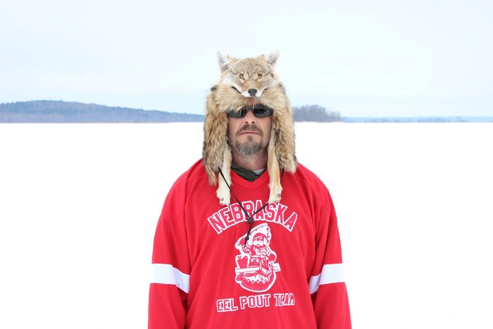 Man wearing a wolf hat and a red Nebraska Eel Pout Team jersey in a snowy landscape.