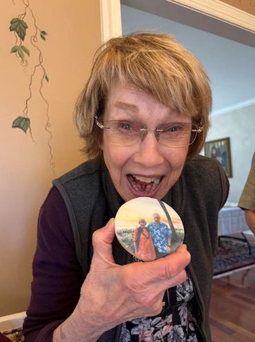 Elderly woman excitedly shows a photo button with a couple's picture.