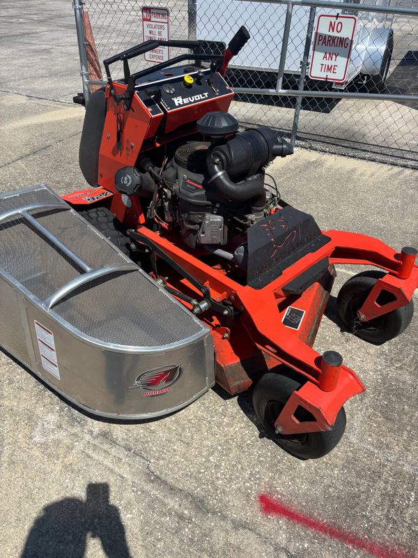 Red Revolt zero-turn lawn mower with a metal grass catcher on pavement.