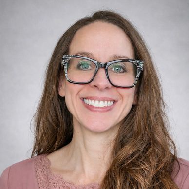 Smiling woman with long brown hair and large glasses.