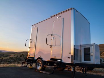 Two portable restroom trailers parked outdoors at sunset.