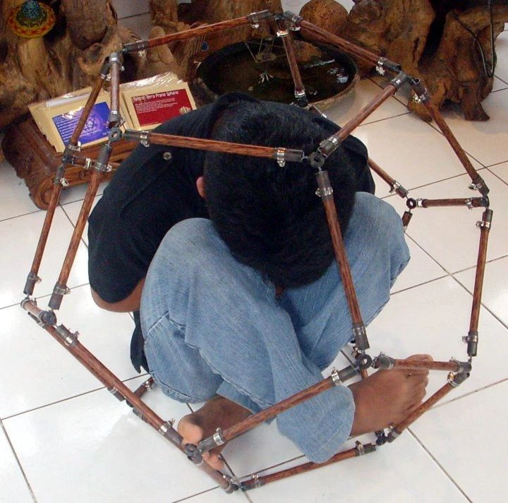 Person curled up inside a geometric wooden frame.