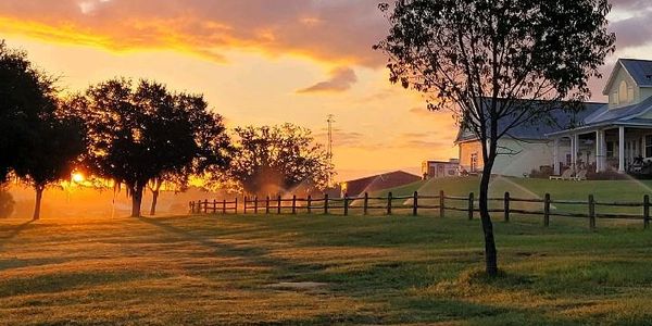Sunset over a peaceful countryside with trees and a house.