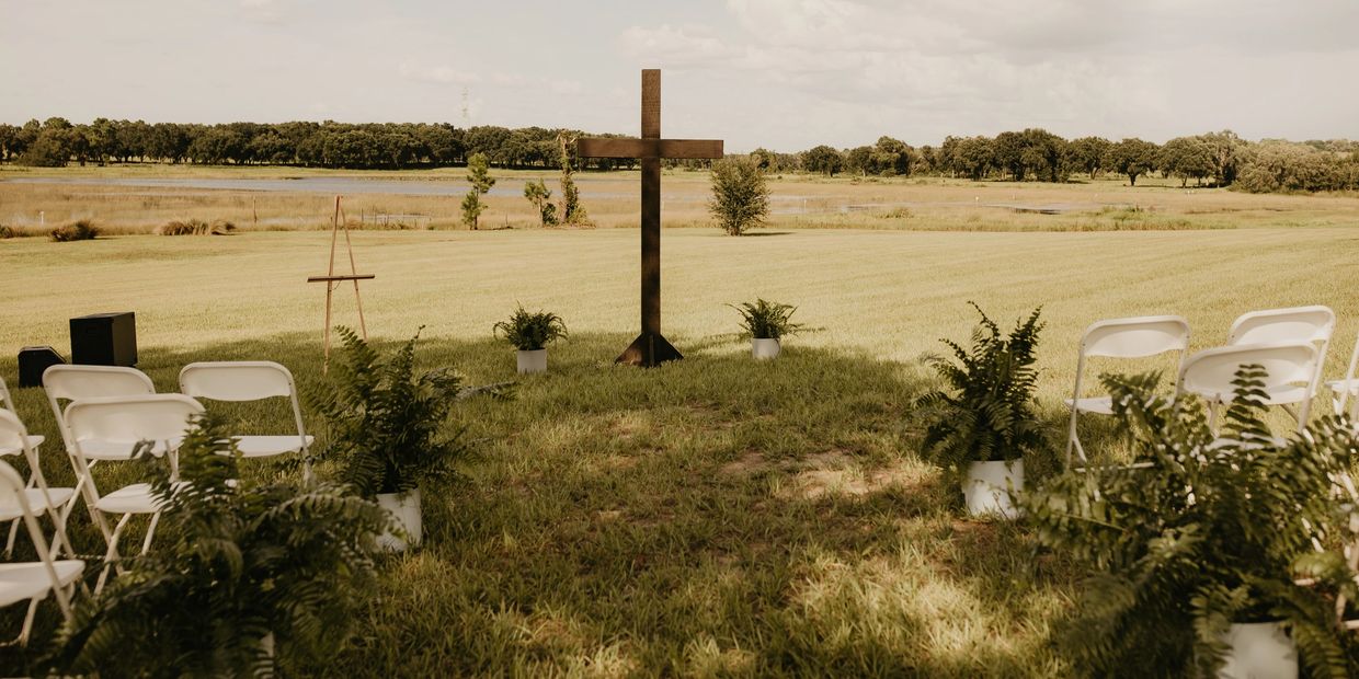 Outdoor ceremony setup with white chairs and a wooden cross by a lake.