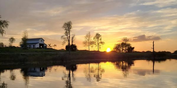 Sunset reflecting on a calm lake with a house and trees.