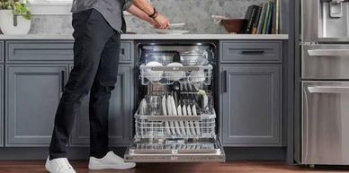 Person loading dishes into an open dishwasher in a modern kitchen.