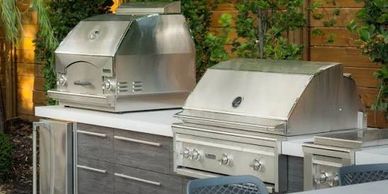 Modern outdoor kitchen with stainless steel grills and wooden cabinetry.