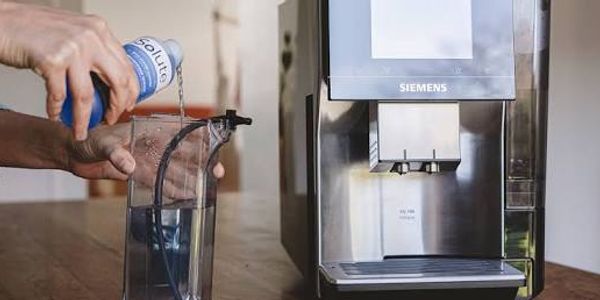 Person pouring descaling solution into a Siemens coffee machine water tank.