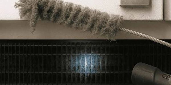 A dusty brush and flashlight near a vent filled with dust and debris.